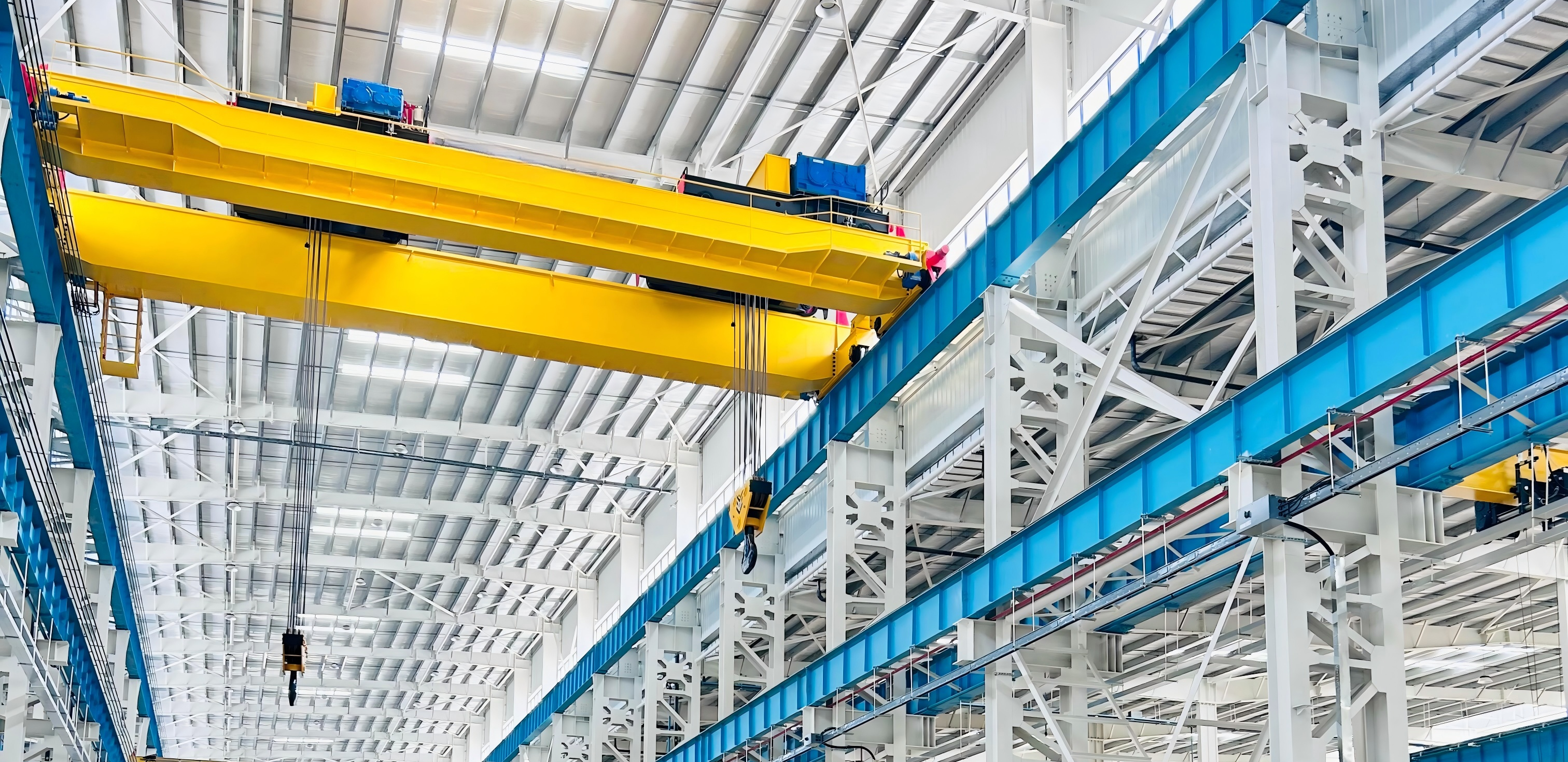 Yellow double girder bridge crane on parallel elevated runway rails in a bright industrial workshop
